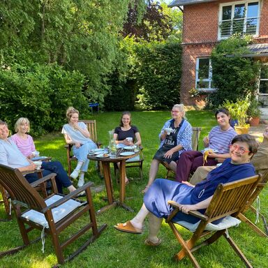 Fröhliche Teilnehmerinnen eines Schmuck Workshops von Gabi Veit sitzen im Kreis bei der Mittagspause im schattigen Garten