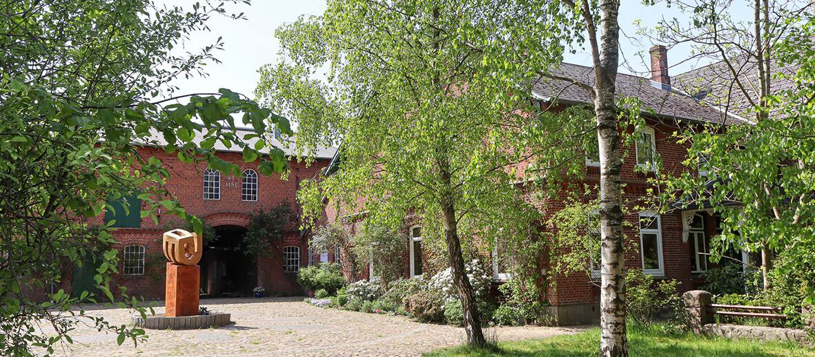 Gutshof mit Skulptur in der Einfahrt, umgeben von Bäumen